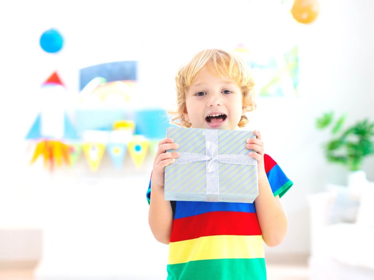 A young boy wearing a multicoloured striped top holding a wrapped birthday present