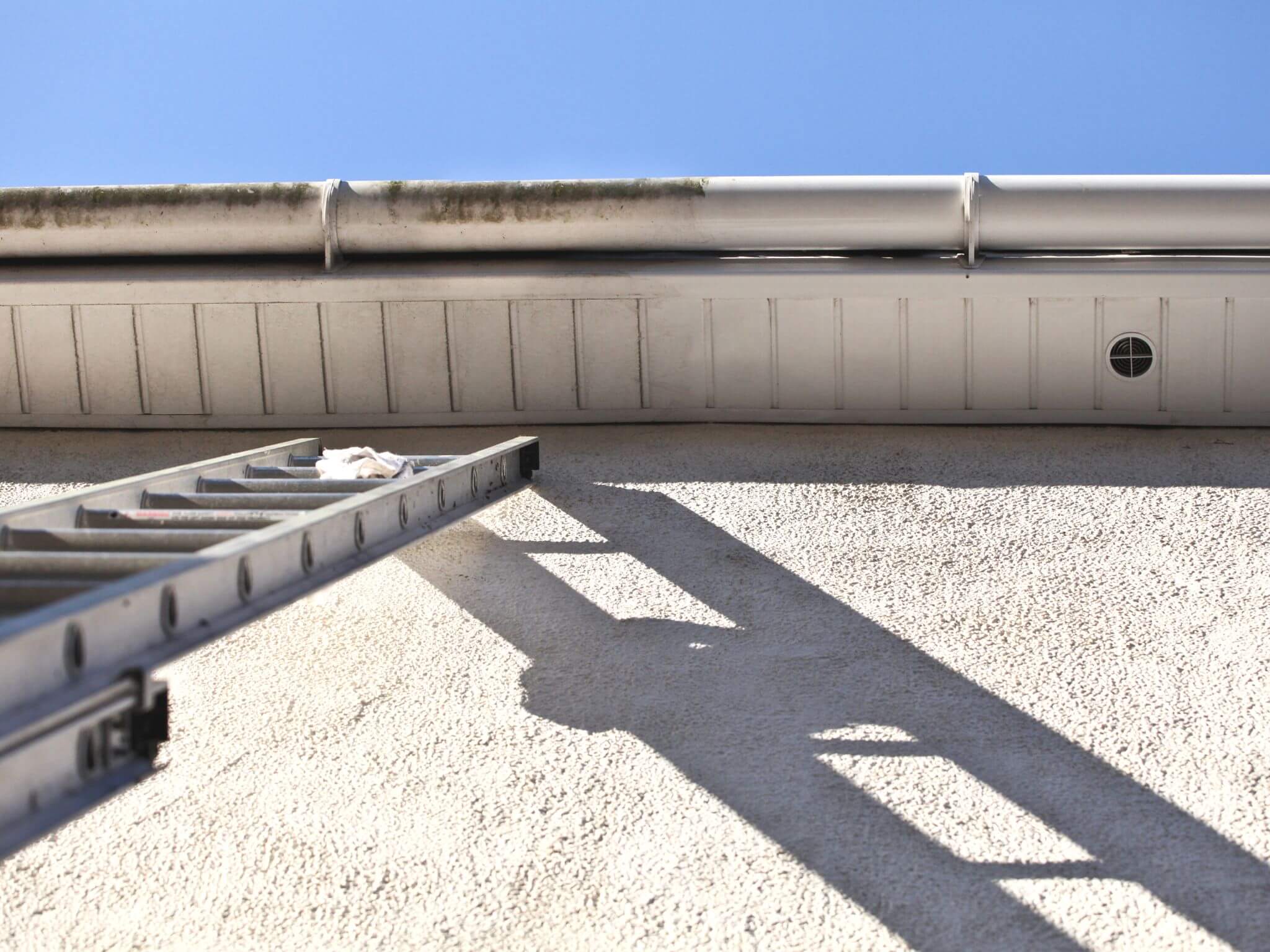 A ladder resting up a house wall with a view of the gutter and soffits.