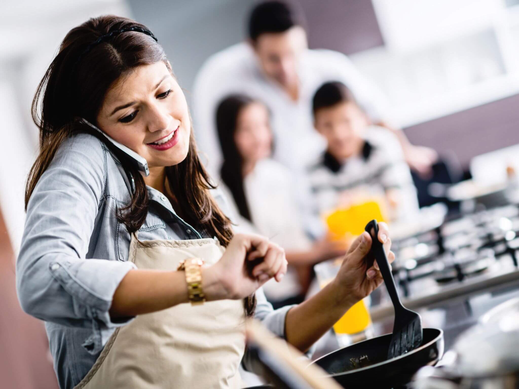A busy mum multitasking in the kitchen. She is cooking dinner and taking a phone call.