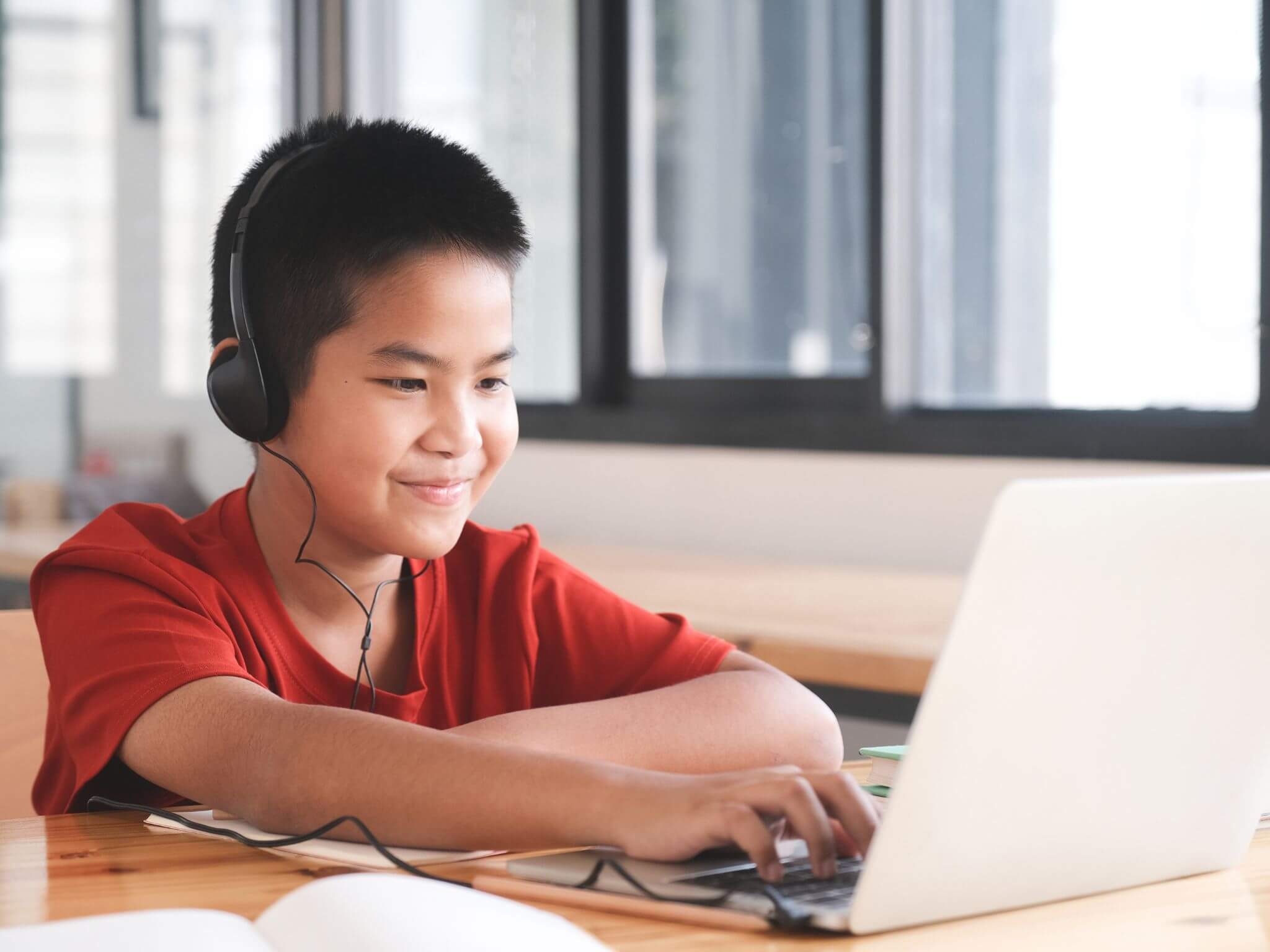 A junior aged boy using a laptop and wearing black headphones.
