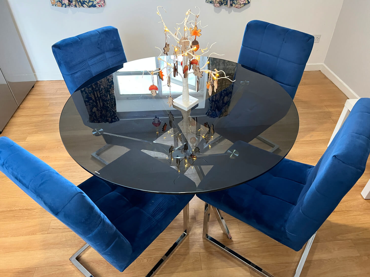 A round grey glass table with four royal blue velvet chairs with chrome legs.