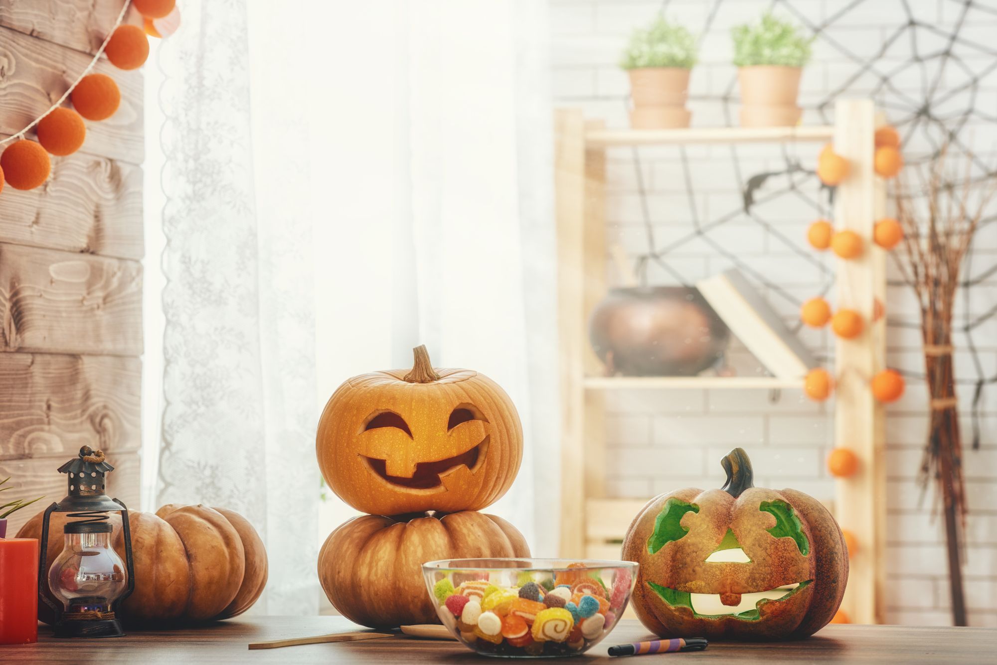 A kitchen with carved pumpkins on the worktop. There is also a glass bowl full of candy and a spider's web decoration hanging on the wall.