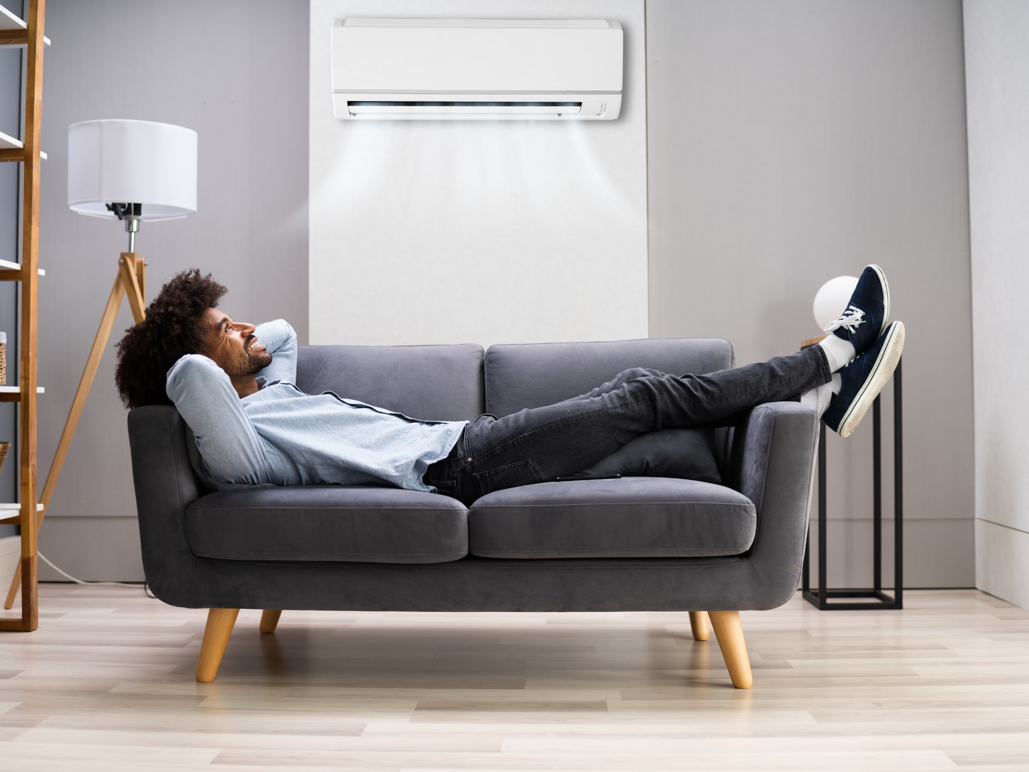 A guy lying on the sofa with an air con unit above him.