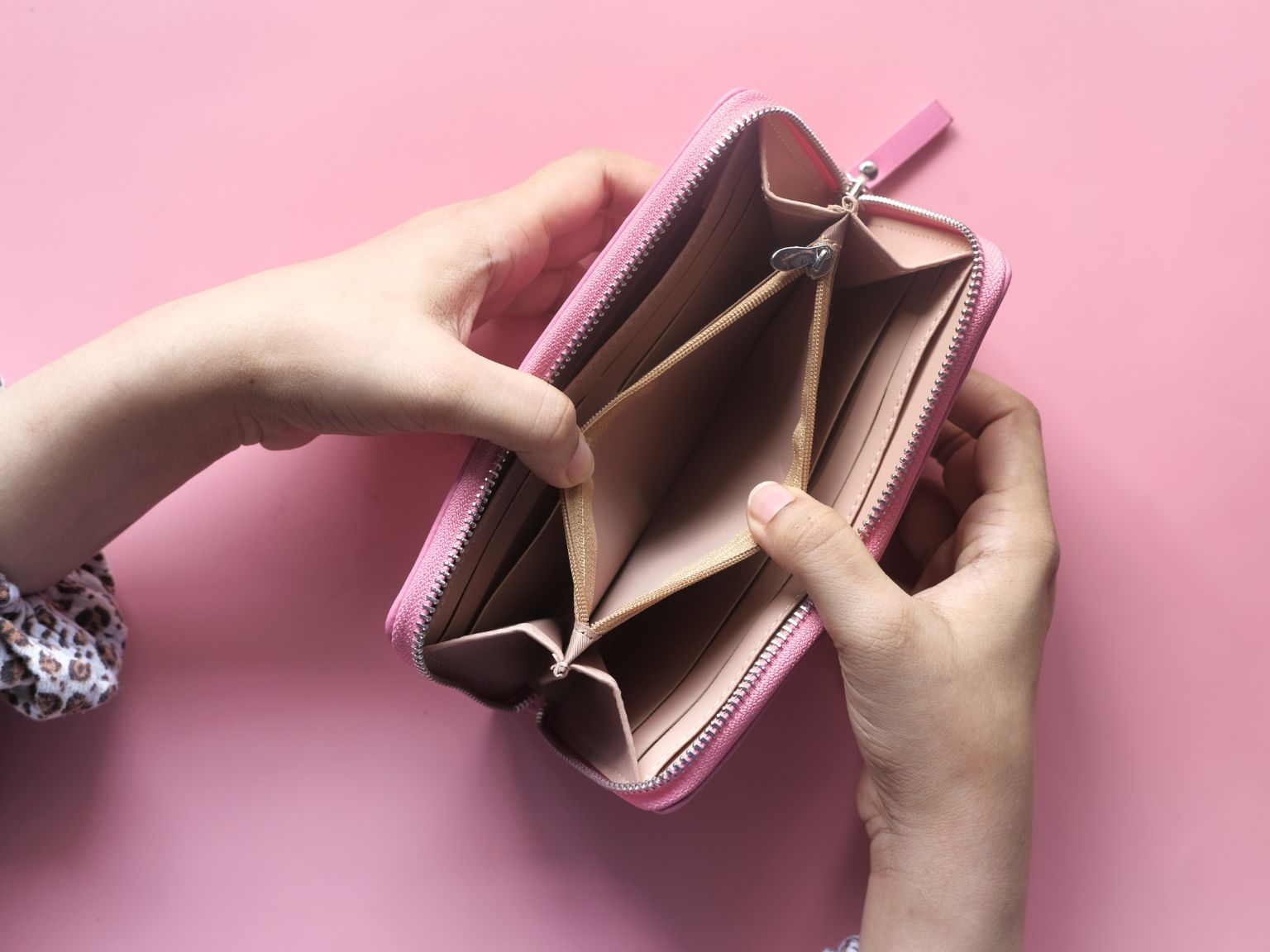 A close-up of a lady's hands opening up her pink empty purse.